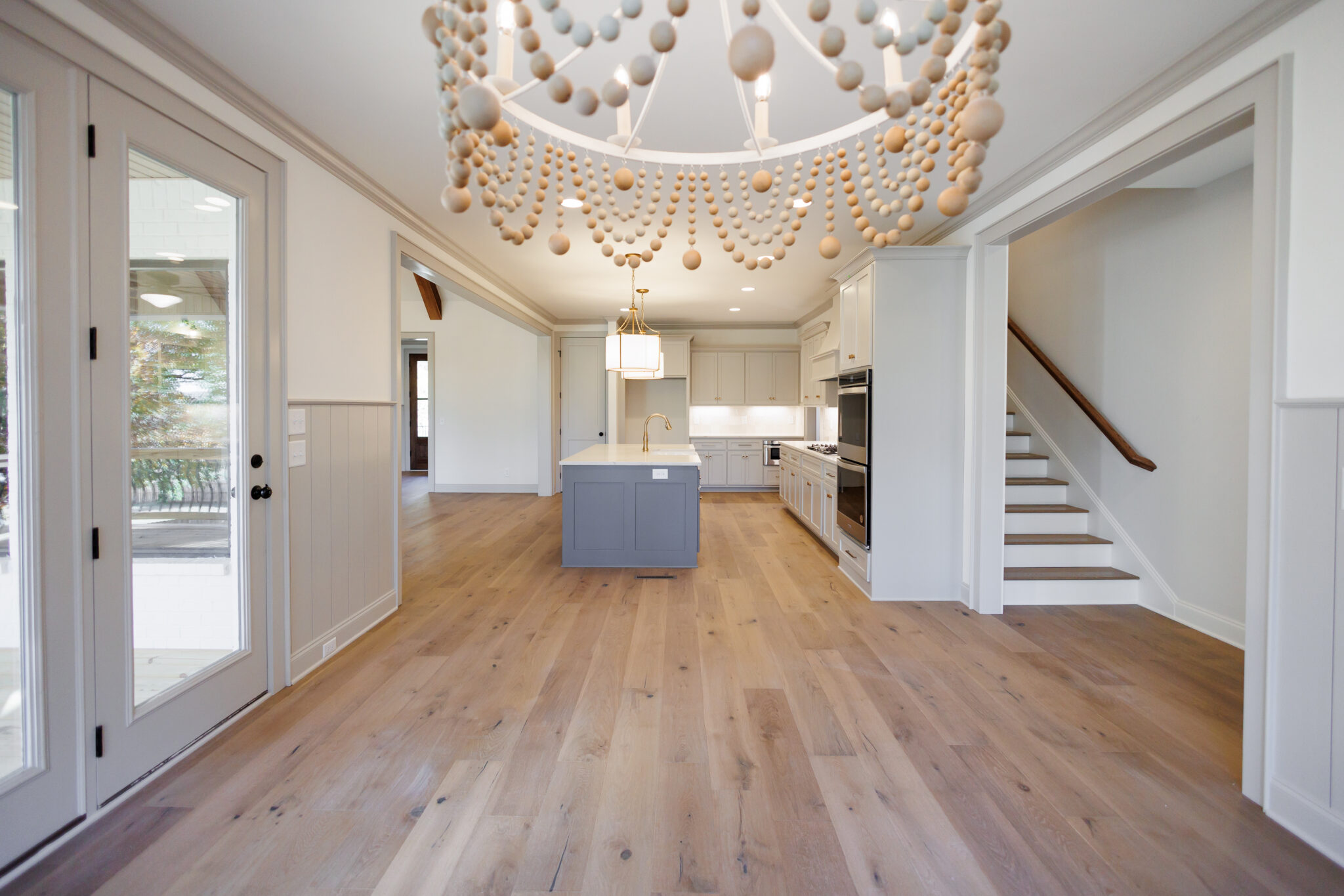 Bright living room with a wood-bead chandelier, white oak floors and an open view to the kitchen
