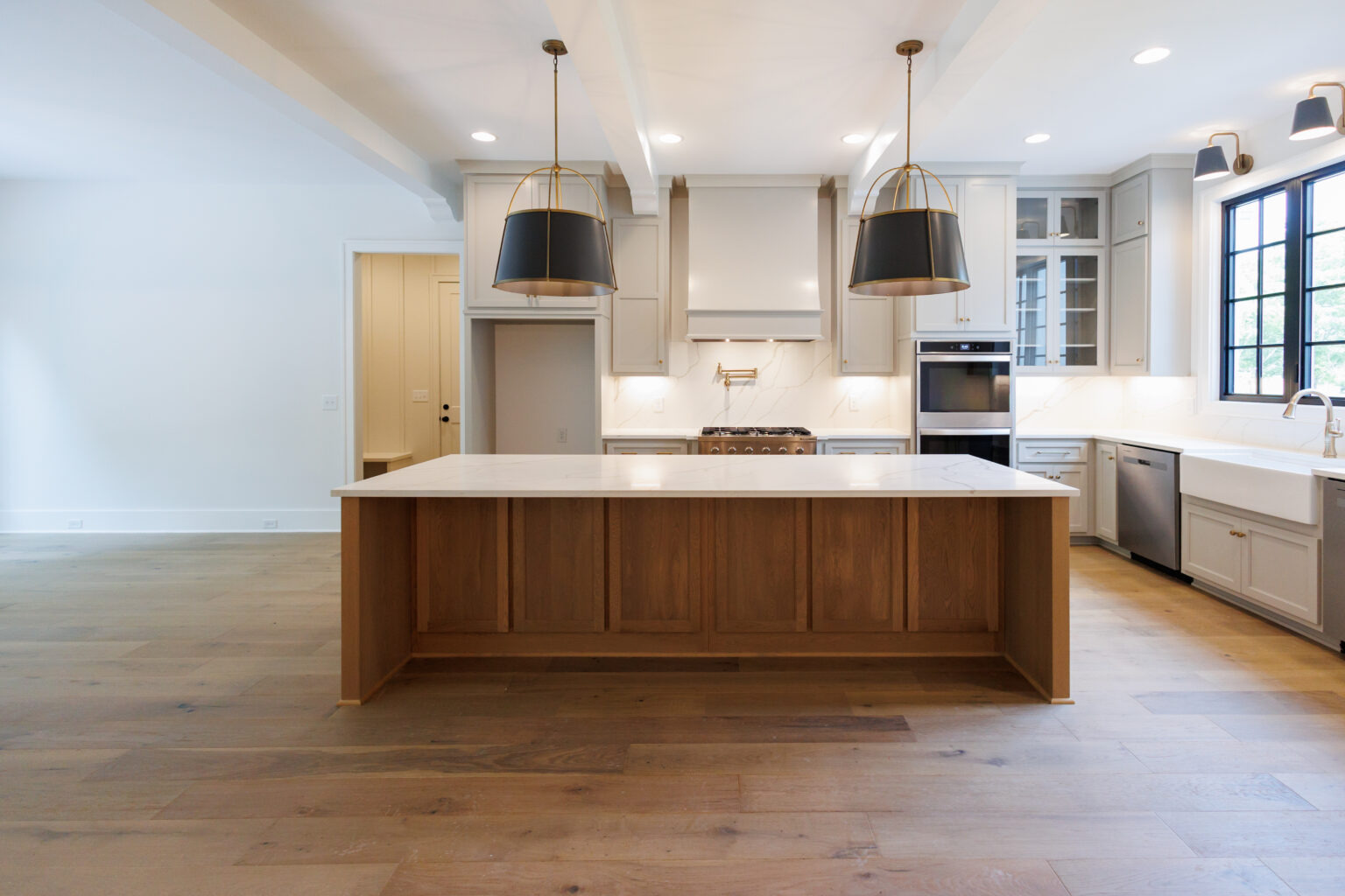 Open kitchen with a large wood island, white countertops and black pendant lights