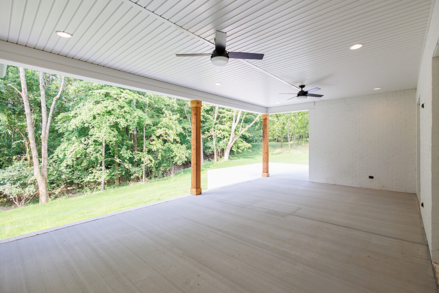 Covered back porch with a tongue-and-groove ceiling, ceiling fans and a view of the trees