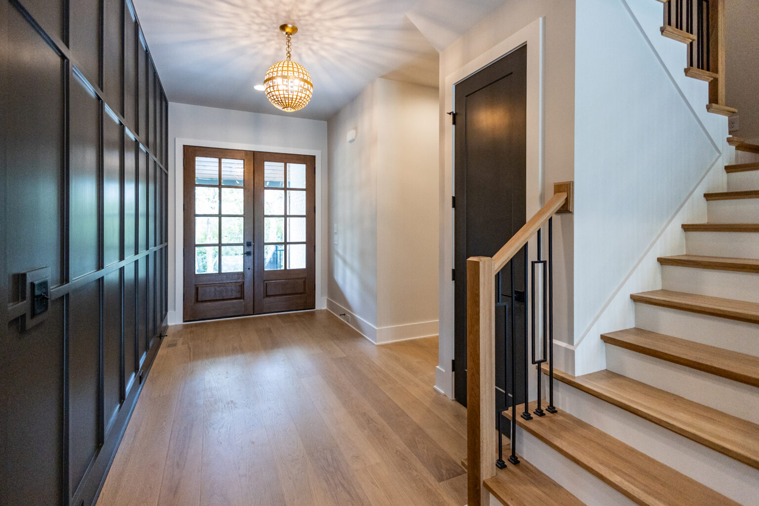 Entry foyer with wood double doors, a staircase with white oak treads and a brass pendant