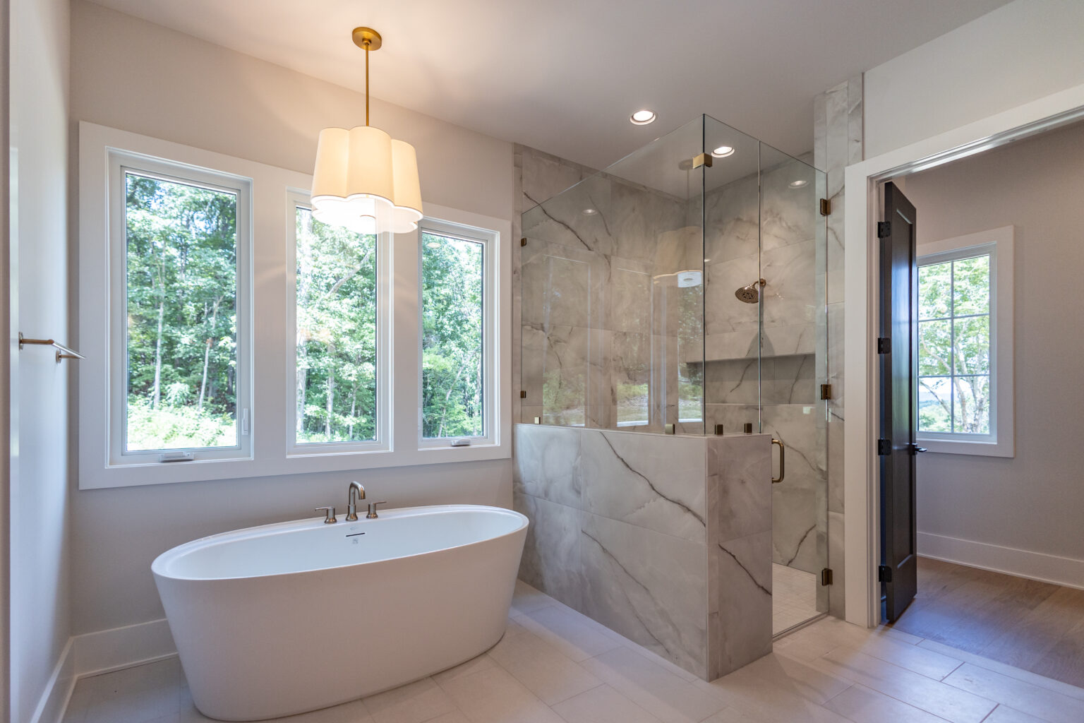 Primary bathroom with a freestanding tub, brass pendant light and marble-look shower